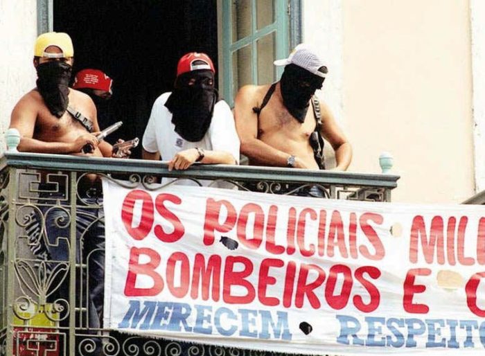 Hooded police officers on strike standing guard at a balcony during a clash with Brazilian troops in downtown Maceio