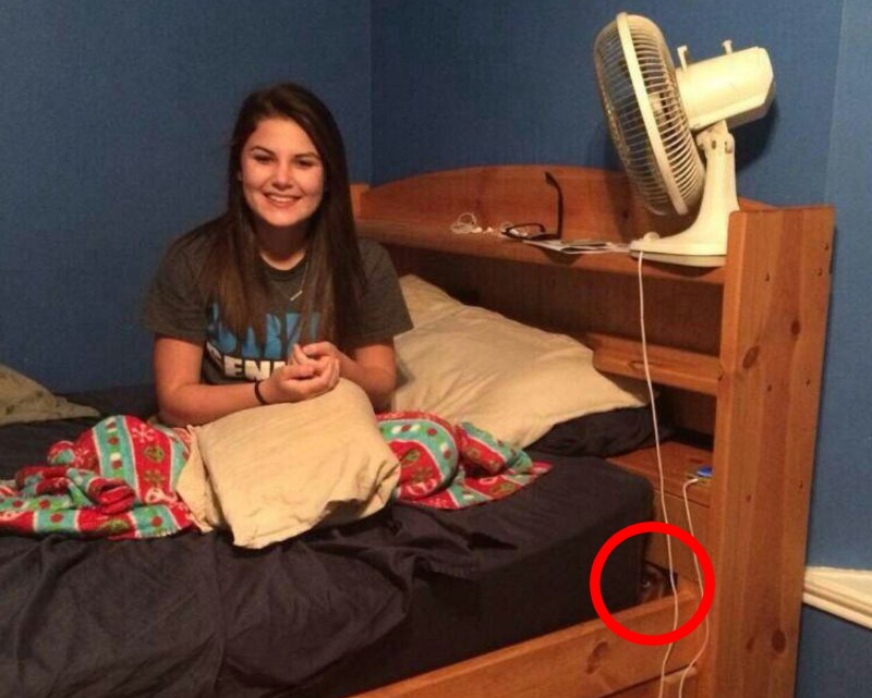 Chica sentada sobre su cama sonriendo, mientras una cara se asoma por debajo