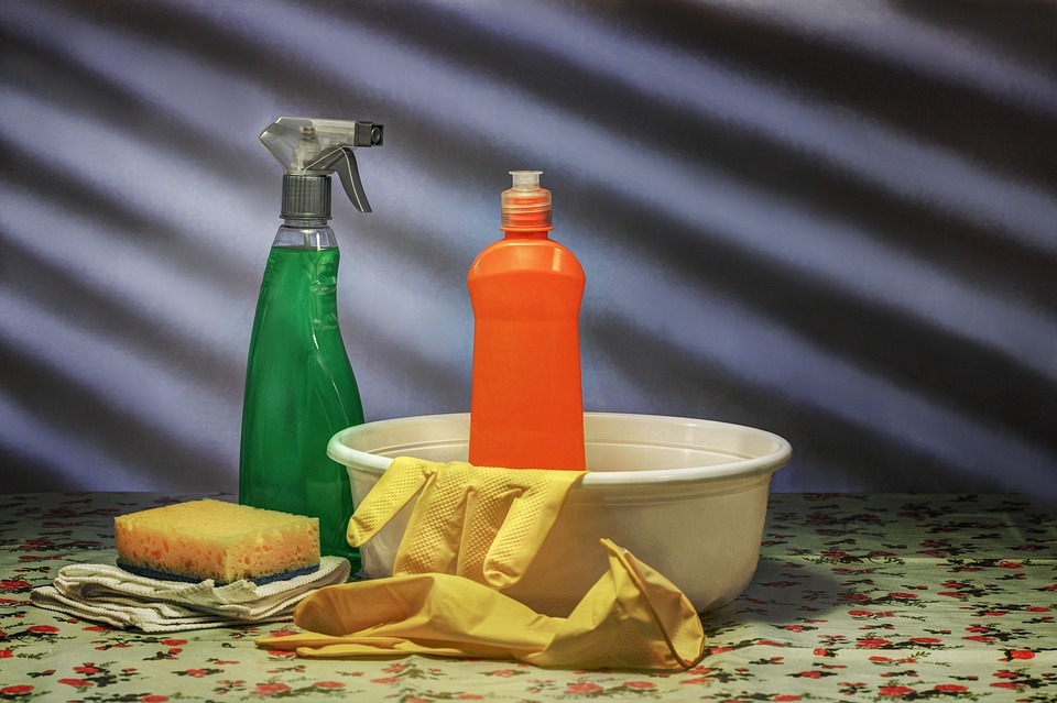 Desinfectantes, guantes amarillos, taza y esponja sobre una mesa