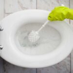 Persona con guantes amarillos lavando el inodoro con un cepillo